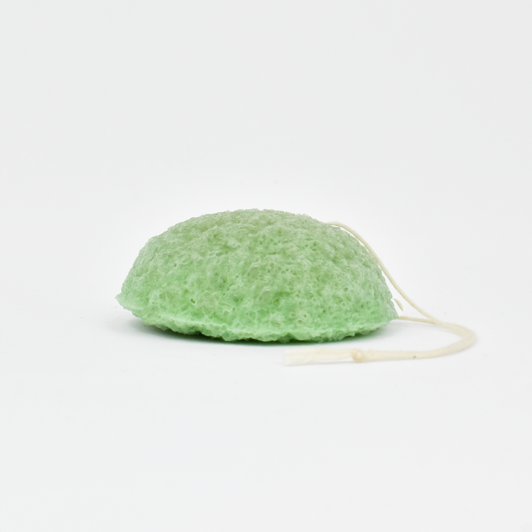 A green plant-based konjac sponge, also known as a matcha sponge, with a soft, textured surface and a string attached for use as a skincare tool.