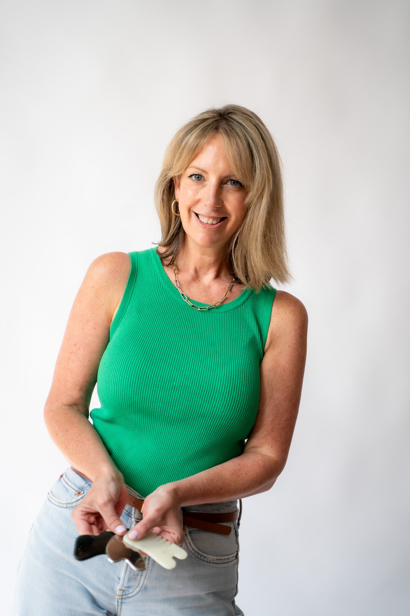 Woman in a green sleeveless top holding a brush against a white background