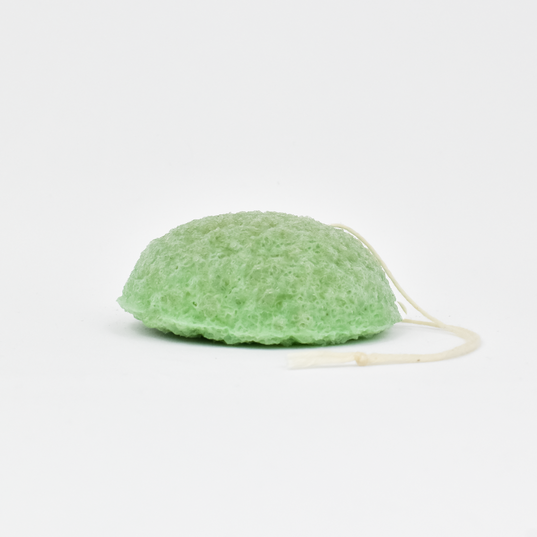 A green plant-based konjac sponge, also known as a matcha sponge, with a soft, textured surface and a string attached for use as a skincare tool.