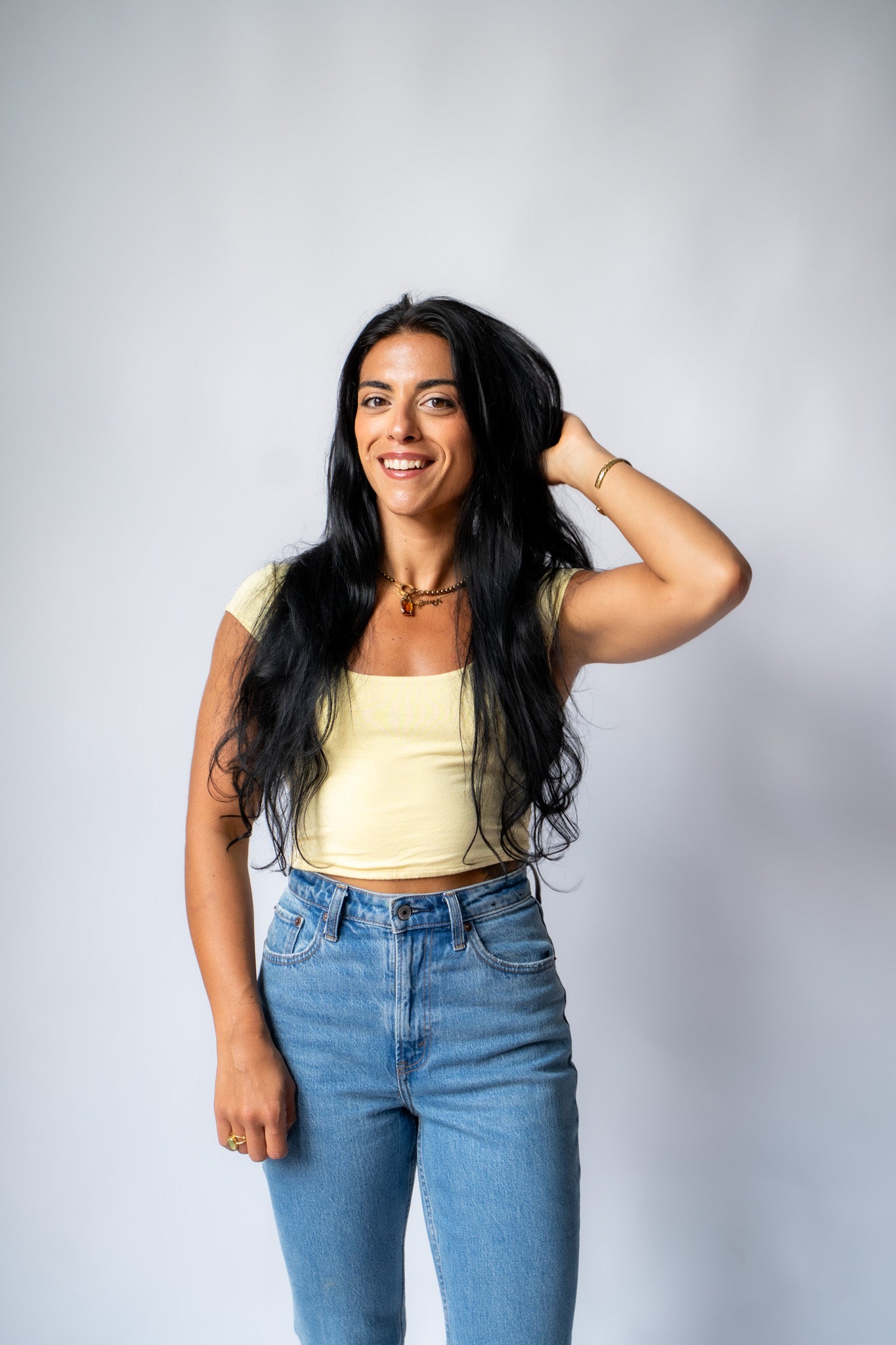 Woman wearing a yellow top and blue jeans against a gray background