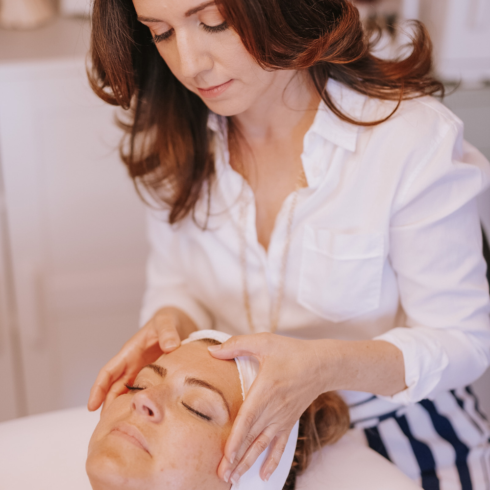 Woman receiving a facial treatment from another woman in a white shirt.