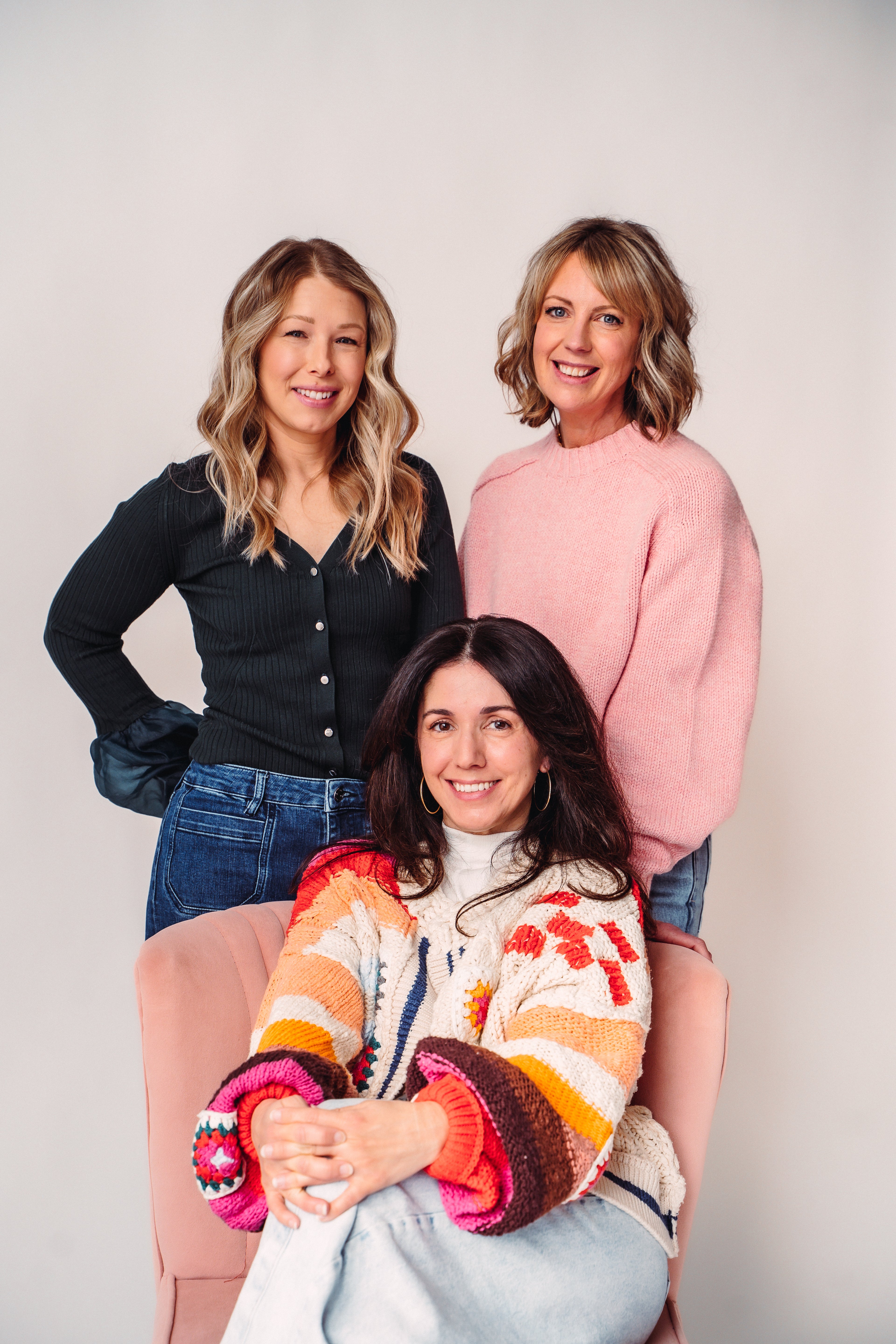 Three women standing together against a plain background